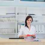 Young practitioner doctor working at the clinic reception desk, she is answering phone calls and scheduling appointments