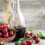 Kirsch liquor in a glass bottle on wooden table. Sweet alcohol made from cherry fruits