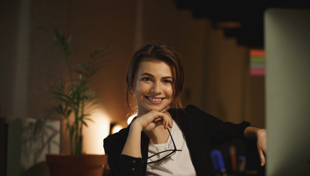 Happy young woman designer sitting in office at night
