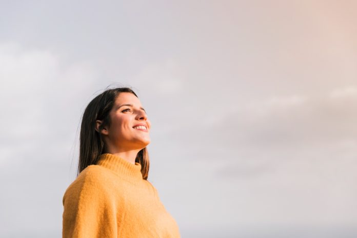 smiling-young-woman-standing-against-sky-looking-away