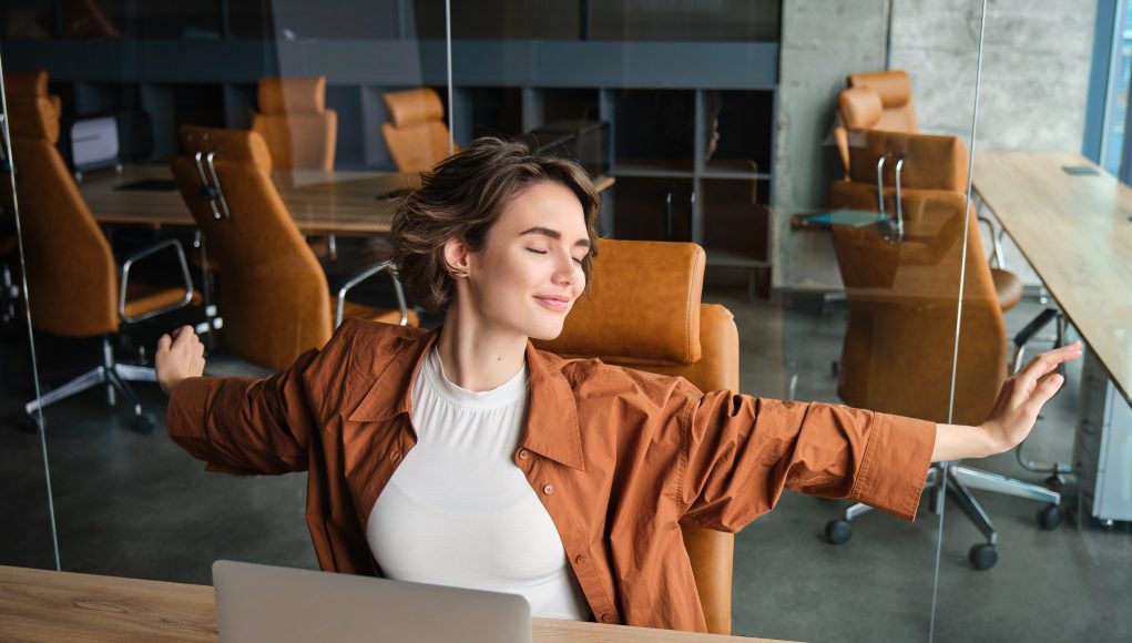 Portrait of woman resting in office, stretching arms after sitting and working on laptop