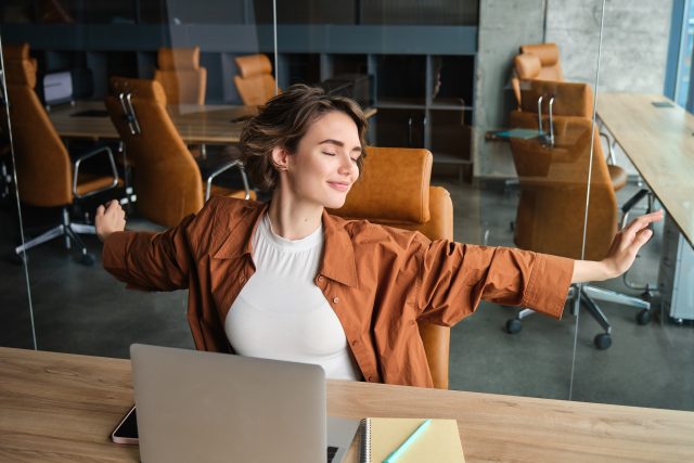 Portrait of woman resting in office, stretching arms after sitting and working on laptop