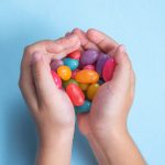 Child’s hand holding several Jelly Beans over blue background