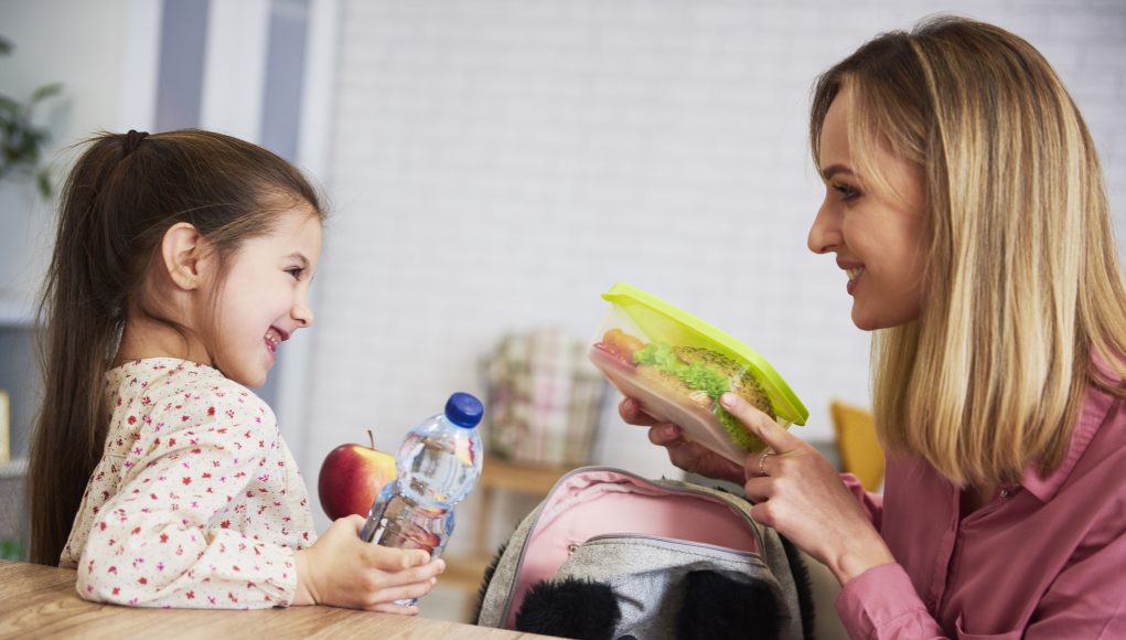 Mum putting lunch box with healthy food in backpack