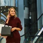 Pretty cheerful blond girl in knitted sweater happily talking on