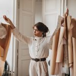 woman thoughtfully looking at her clothing patterns. Young lady in beige blouse and pants working o