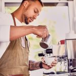 Black bearded coffee seller pouring coffee.