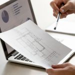 Male hand holding project plan, statistics on screen, close up